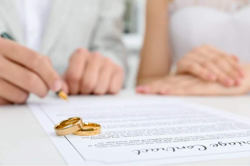 Mesa de trabajo con manos firmando pactos matrimoniales y documentos legales.